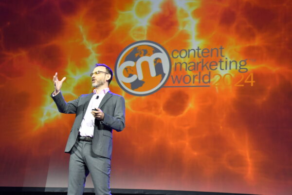 Seth Stephens-Davidowitz is standing on stage wearing a gray suit and a pink button-down suit. The back is the Content Marketing World 2024 logo.