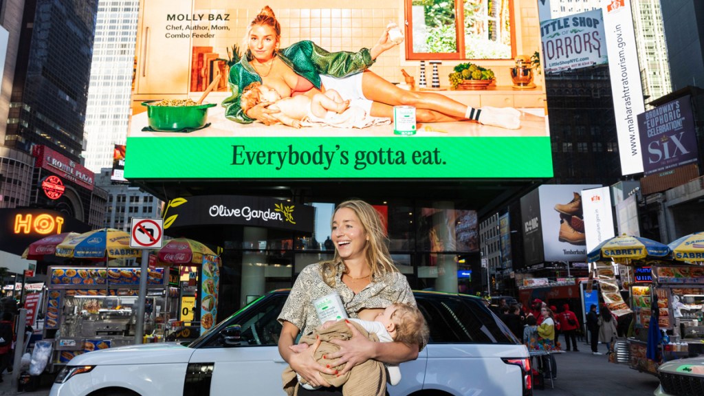 Woman breastfeeding a baby in front of an advertising billboard