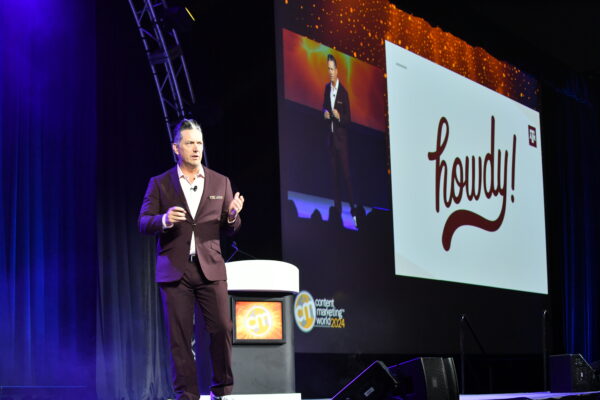 R. Ethan Braden standing on stage in a black suite and white button-down shirt. The slide in the background says "Hi!"