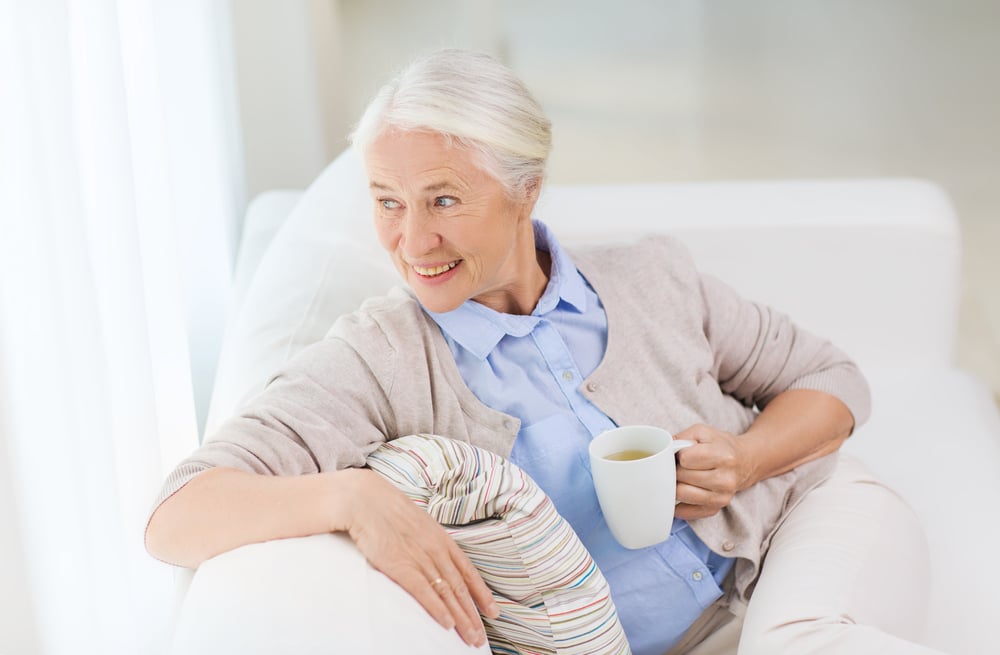 An elderly woman relaxes on the sofa with a cup of tea